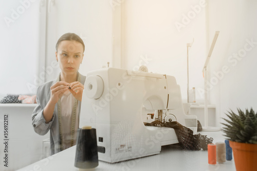 Picture of young woman tailor working on a sewing machine with sun reflection photo