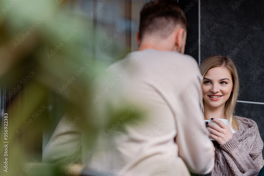 selective focus of happy woman holding cup and looking at man outside