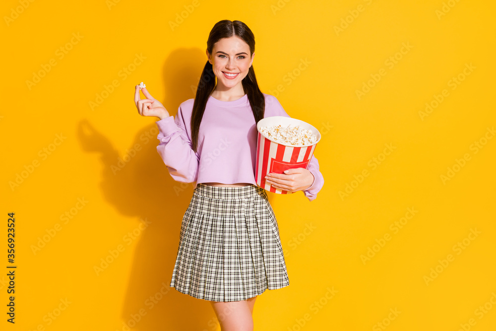 Portrait of cheerful lovely teen girl watch movies hold eat big striped pop corn box wear plaid jumper isolated over bright color background Portrait of cheerful lovely teen girl watch movies hold eat big striped pop corn box wear plaid jumper isolated over bright color background