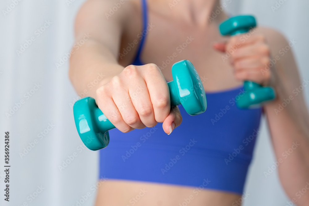 Young woman exercising at home in blue sports top using dumbells Young woman exercising at home in blue sports top using dumbells