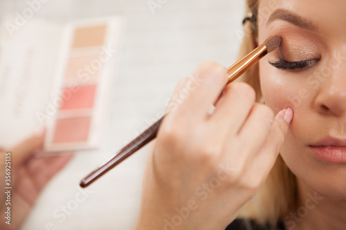 Cropped shot of a makeup artist applying eyeshadow from the neutral palette on eyelids of a beautiful woman