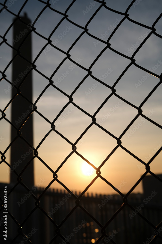 Tall chimney, smokestack, viewed through chainlink fence at dusk Tall chimney, smokestack, viewed through chainlink fence at dusk
