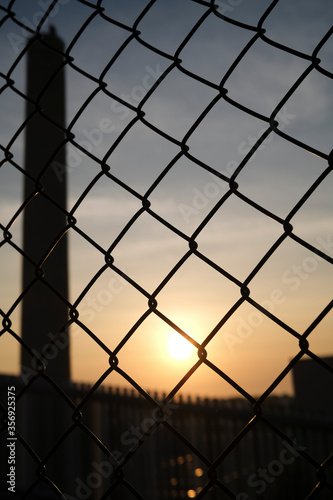 Tall chimney, smokestack, viewed through chainlink fence at dusk