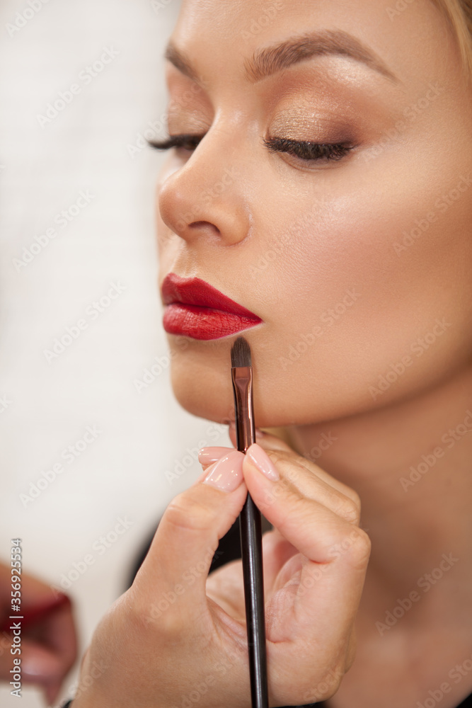 Vertical shot of a makeup artist applying red lipstick on the lips of a female client