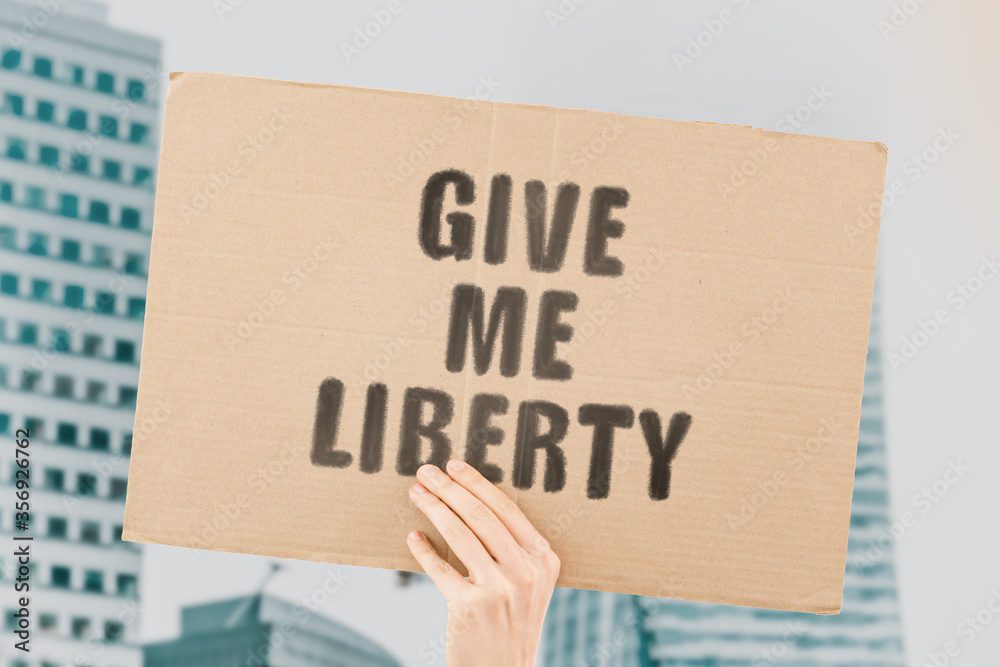The phrase " Give me liberty " on a banner in men's hand with blurred background. Economic freedoms. Economy. Liberal protest on the street. Free people. Taxes
