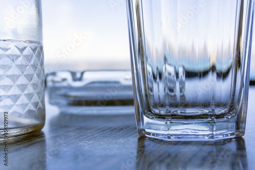 Close up of glass utensils on table. Lights and shadows on glass edges. Wide glass, bottle and ashtray. Pastel monochrome colors.