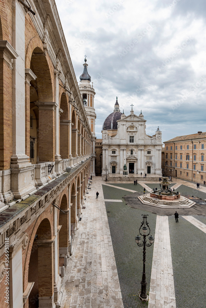Italy, Loreto,square of Loreto with background the basilica with cloudy sky, portico to the side, perspective photo