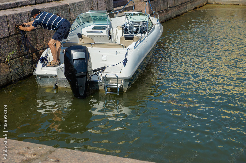 Fototapeta premium Man fastens a motor boat to a quay wall