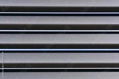 Symmetrical horizontal pattern of metal curved planks of fence. Light and shadow lines. Architecture, design, decorative construction materials. Texture and background.