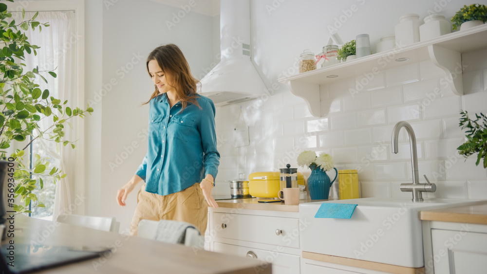 Attractive Young Female in Jeans Shirt and Brown Pants is Creatively Dancing in the Kitchen. Sunny Modern Kitchen with Healthy Lifestyle Vibes. Happy Beautiful Girl Relaxing at Home.