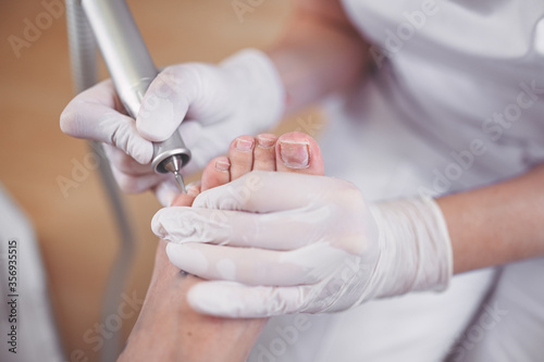 Hardware medical pedicure with nail file drill apparatus. Patient on pedicure treatment with pediatrician chiropodist. Foot peeling treatment at spa with a special device. Clinic of Podiatry Podology photo