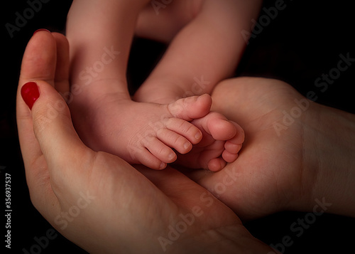 feet of a newborn baby in the hands of a mother on a black background
