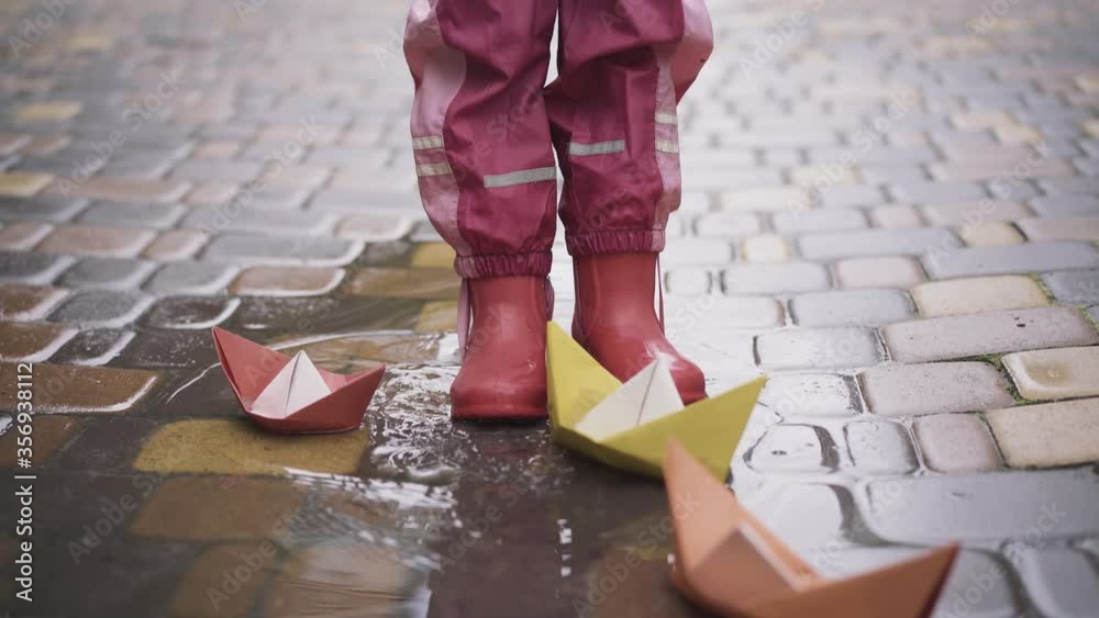 Feet of little girl in rubber boots stomping in puddle with paper boats ...