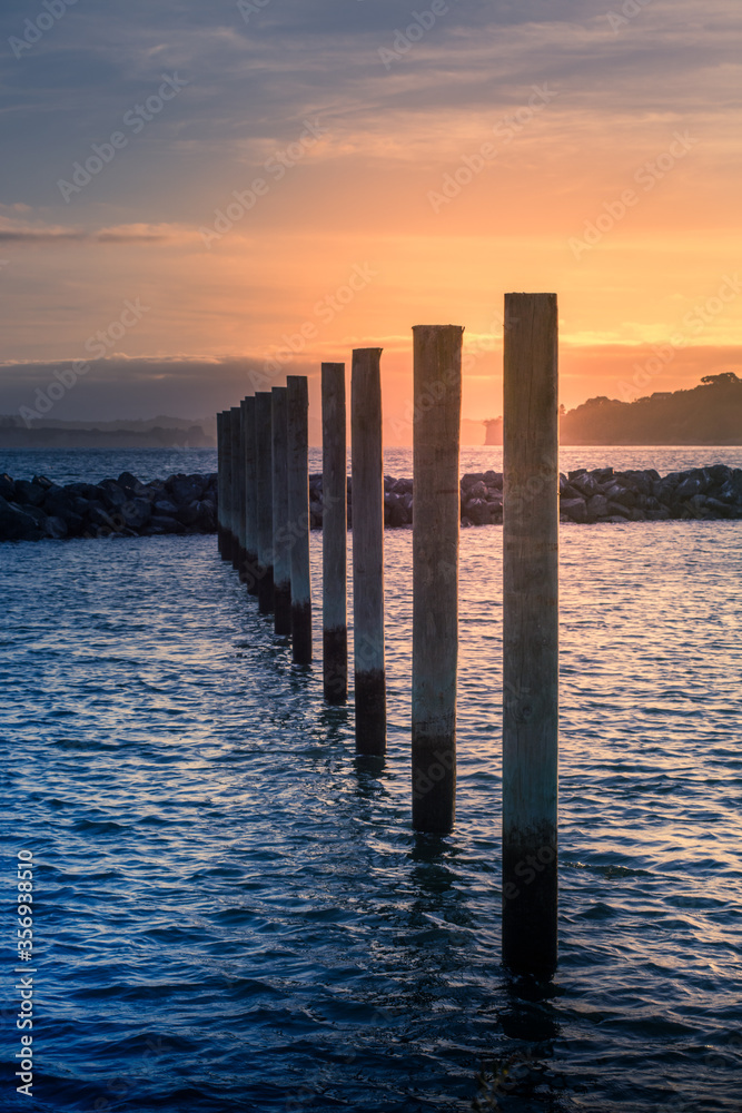 Dramatic sunset over Gulf Harbour marine. Mooring poles lined up towards horizon