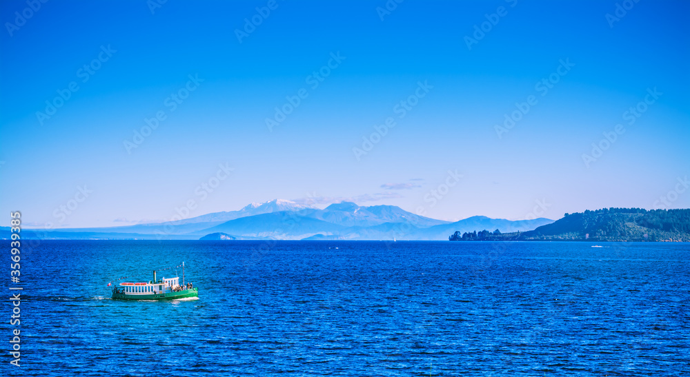 Tourist steamboat crossing the deep blue waters of lake Taupo with Ruapehu mountains in the background on a beautiful sunny day. North Island Volcanic Plateau, New Zealand