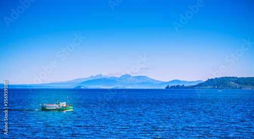 Fototapeta Naklejka Na Ścianę i Meble -  Tourist steamboat crossing the deep blue waters of lake Taupo with Ruapehu mountains in the background on a beautiful sunny day. North Island Volcanic Plateau, New Zealand