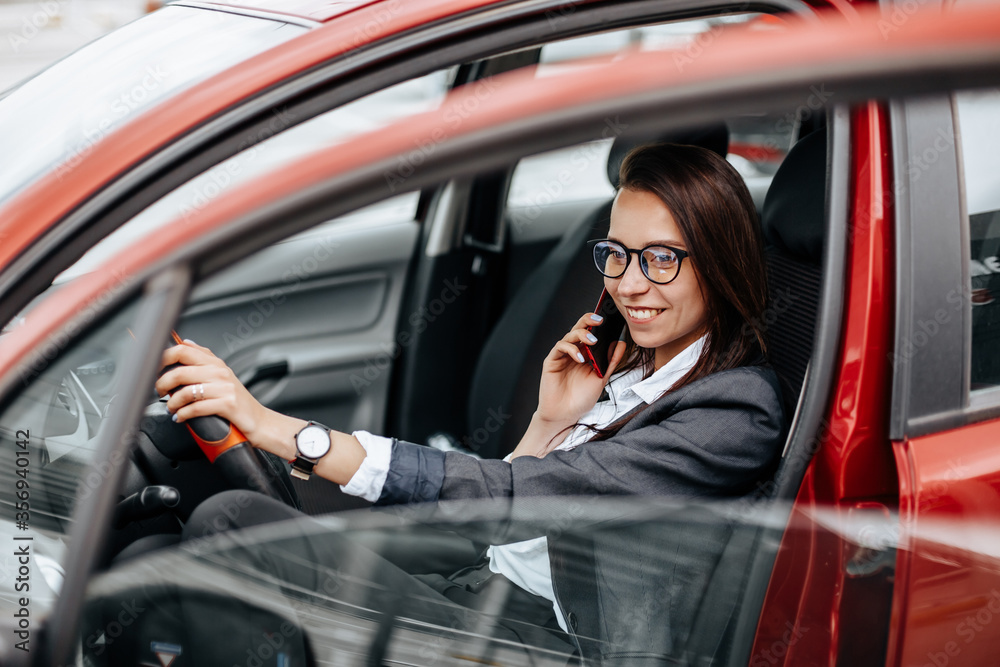 The girl in the car behind the wheel looks at the notification phone and reads the message. A woman in a parking lot sits in a auto. The girl in the car behind the wheel looks at the notification phone and reads the message. A woman in a parking lot sits in a auto.