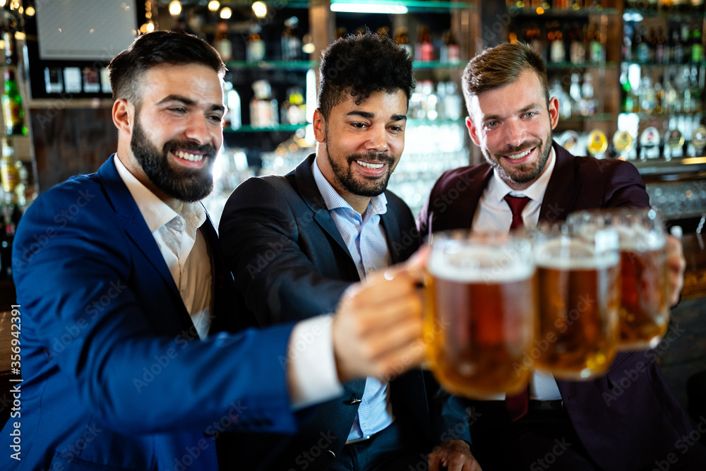 Young businessmen are drinking beer, talking and smiling while resting at the pub