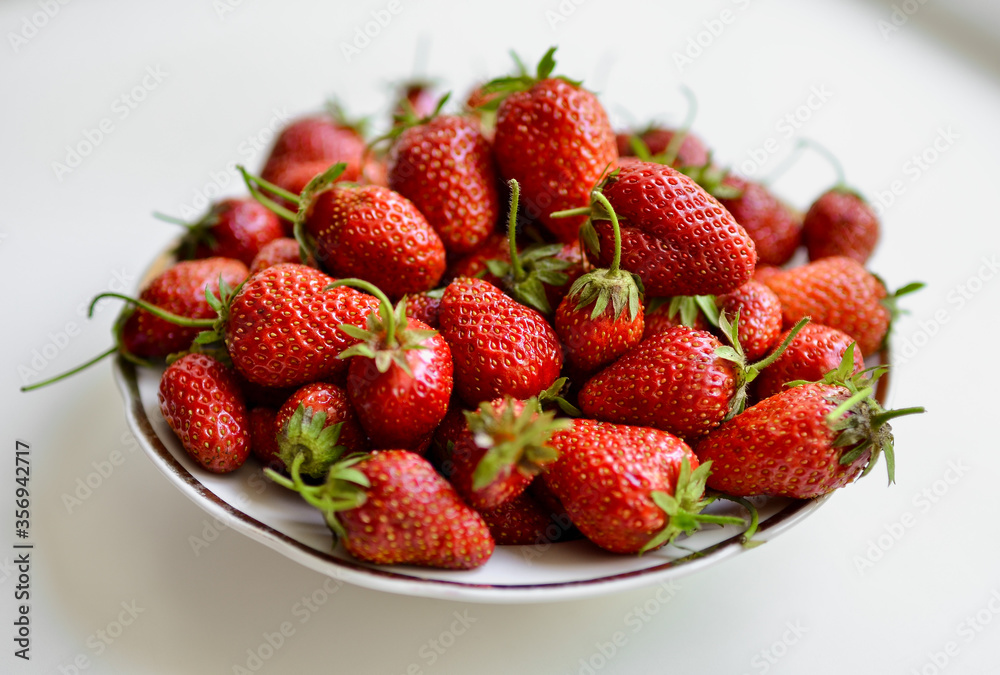 A lot of red, juicy strawberries on a plate. Red berries on a white background. Natural eco-product. A lot of red, juicy strawberries on a plate. Red berries on a white background. Natural eco-product.