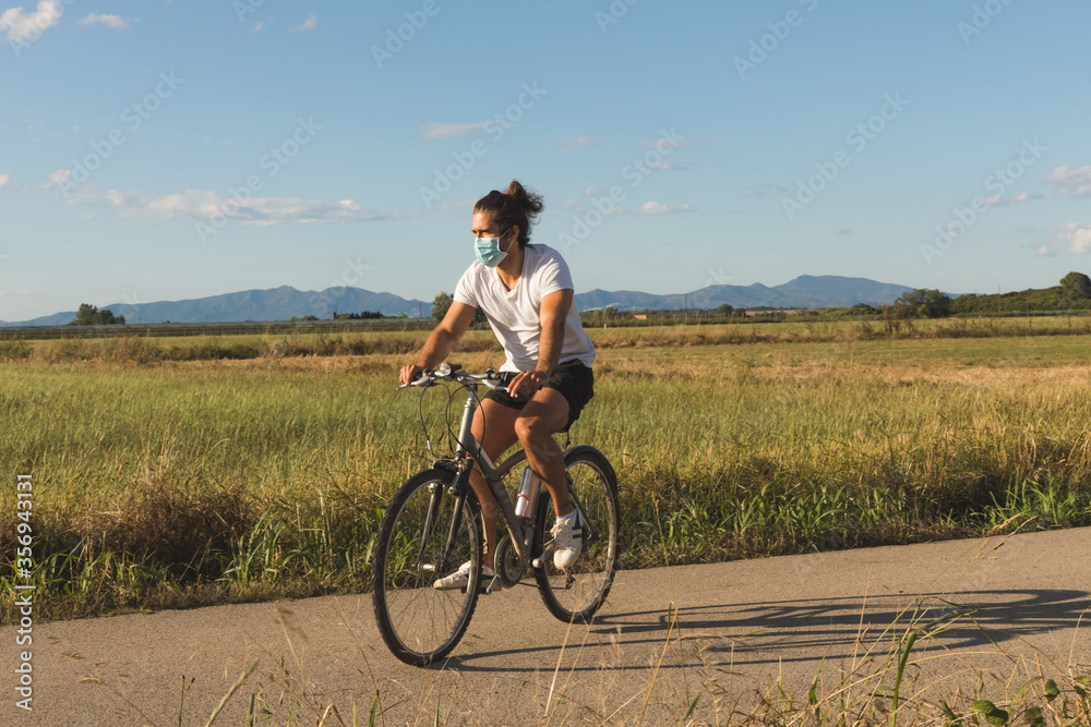 Young man on a bicycle on a country road wearing a mask Young man on a bicycle on a country road wearing a mask