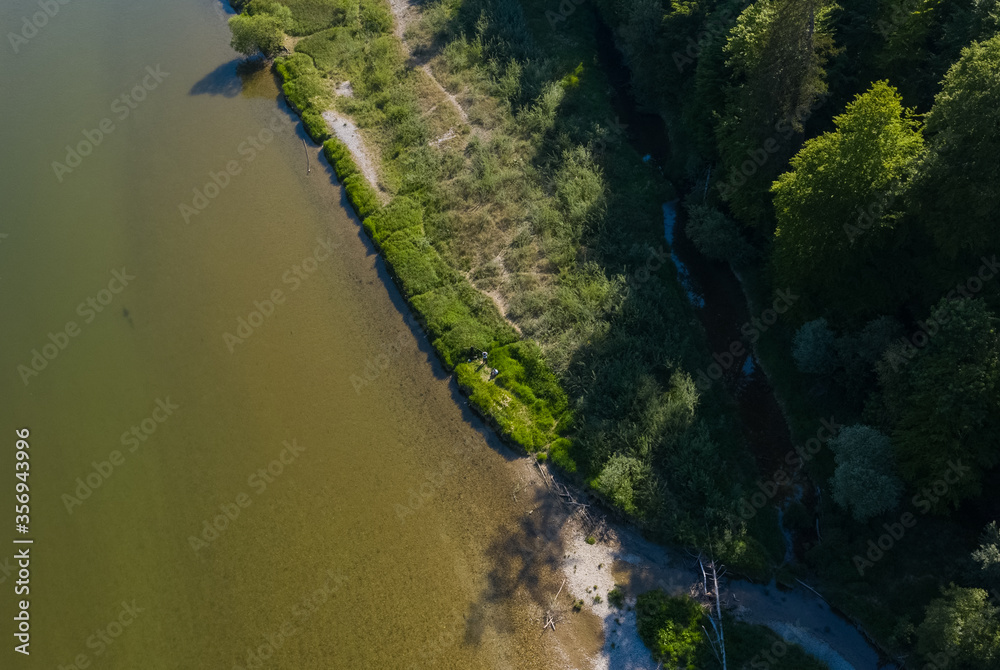 Aerial drone image of water flowing on the Isar river from the Alps to Munich with the shadow of a green forest besides.