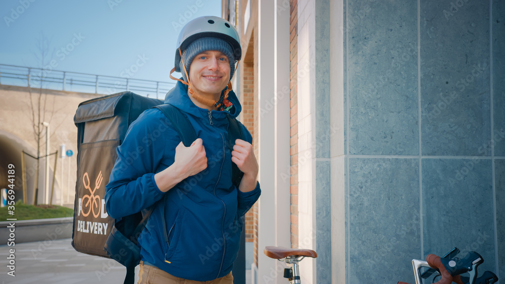 Happy Food Delivery Man Wearing Thermal Backpack on Bike Deliver Restaurant Order. Smiling Courier Looking at Camera. Courier Delivers Takeaway Lunch in Modern City District Office Building. Happy Food Delivery Man Wearing Thermal Backpack on Bike Deliver Restaurant Order. Smiling Courier Looking at Camera. Courier Delivers Takeaway Lunch in Modern City District Office Building.
