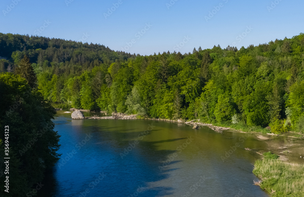 Shadows of a german forest on the Isar river in a spring morning seen from an aerial bird view.