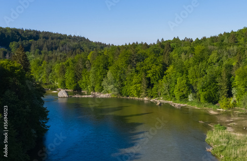Shadows of a german forest on the Isar river in a spring morning seen from an aerial bird view.
