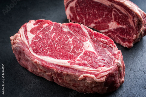 Two raw dry dged Kobe rib-eye steaks as closeup on a black board