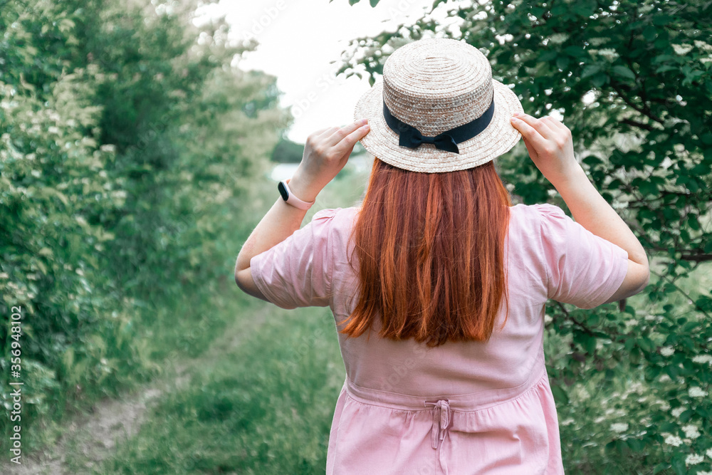 Red haired girl in straw hat in the garden, back view
