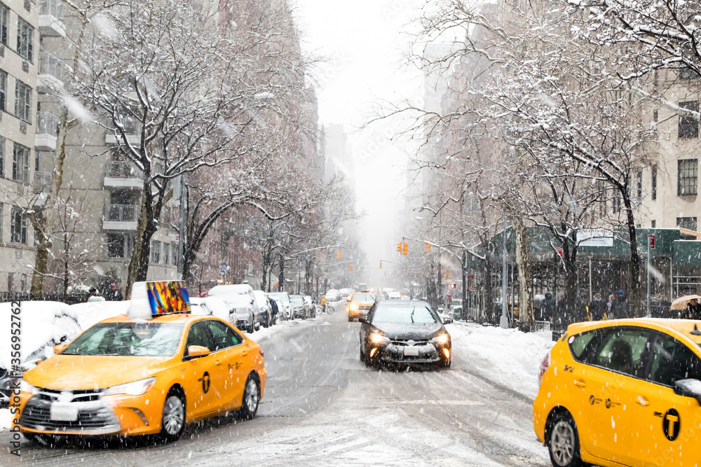 Taxis and cars driving down a snow covered 5th Avenue during a winter blizzard scene in Manhattan New York City