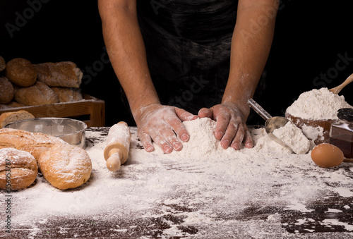 The table is full of flour and equipment for making bread and the chef is preparing the dough. On a black background