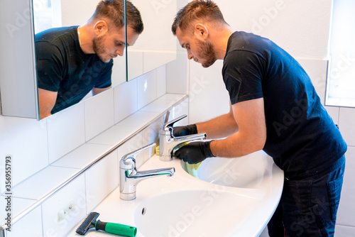man cleaning a bathroom sink with a scraper blade and micro fiber cloth to remove lime and stains