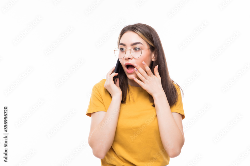 Surprised young woman talking on the mobile phone and pointing finger away isolated on a white background Surprised young woman talking on the mobile phone and pointing finger away isolated on a white background