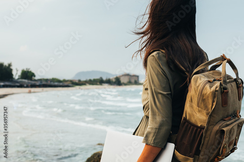 A freelancer girl is standing on the seashore looking at a beautiful seascape.