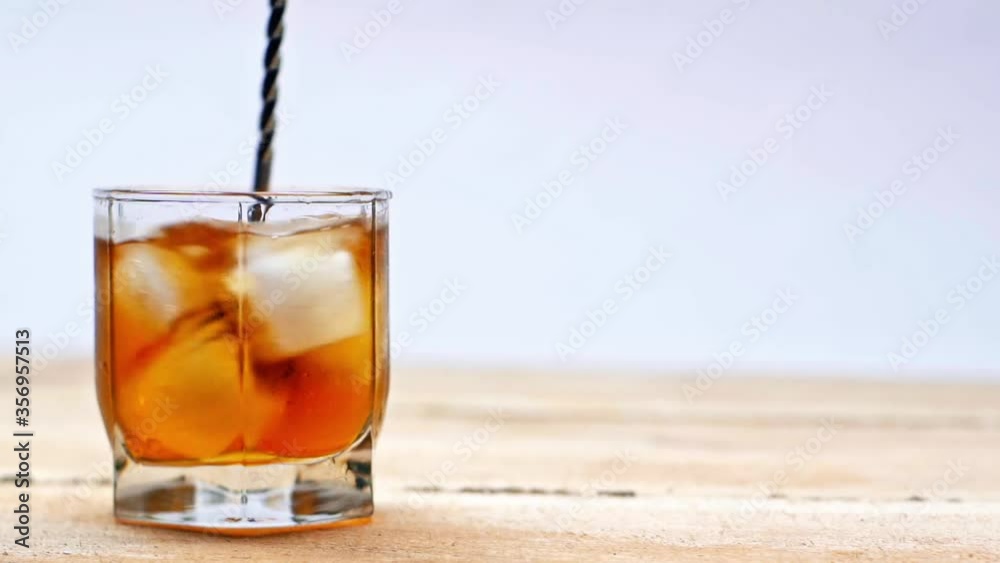 mixing of whiskey and ice cubes in glass with cocktail spoon isolated on white mixing of whiskey and ice cubes in glass with cocktail spoon isolated on white