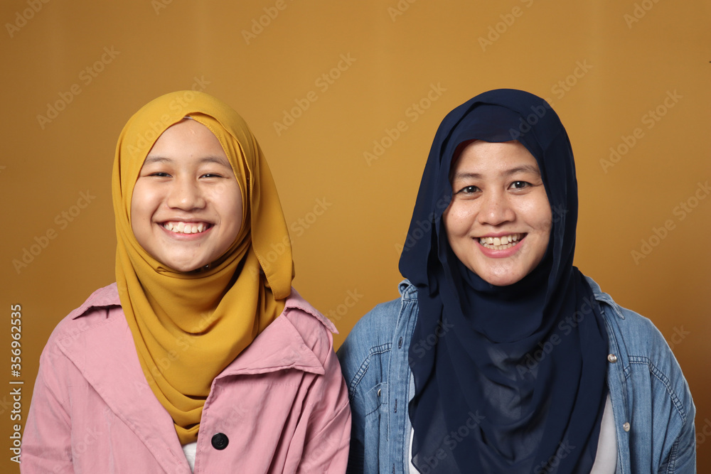 People and family concept - happy smiling Asian muslim mother hugging daughter against yellow background People and family concept - happy smiling Asian muslim mother hugging daughter against yellow background