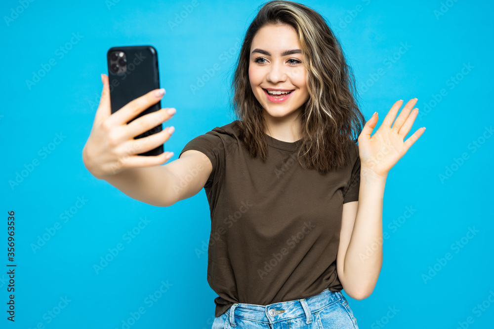 Young cheerful attractive woman have video call wave hello on the camera of her phone isolated on the blue background. Young cheerful attractive woman have video call wave hello on the camera of her phone isolated on the blue background.