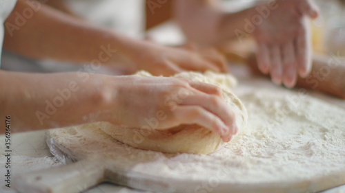 Woman helping daughter to knead dough with flour on kitchen table
