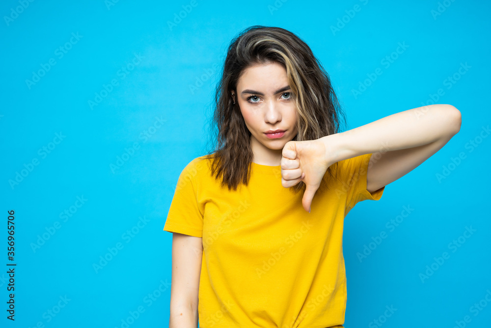 Young beautiful woman with thumbs down isolated blue background Young beautiful woman with thumbs down isolated blue background