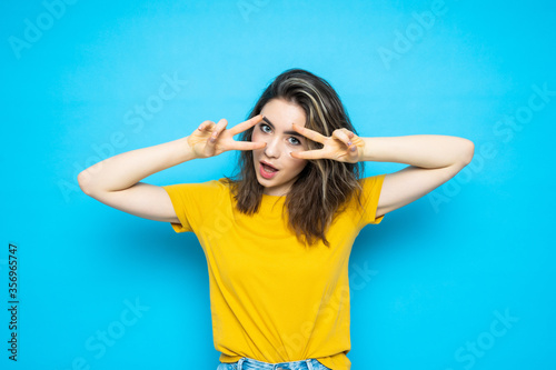 Young lady showing peace gesture standing isolated over blue background.