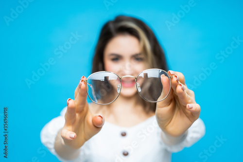 Surprised young girl taking off her glasses isolated on blue background