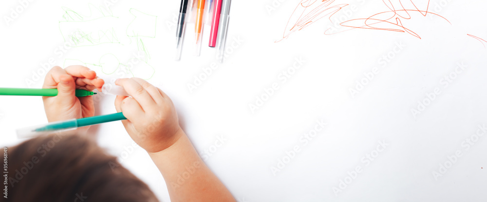 Little child draws on white paper with colored felt-tip pens, teaching children to draw Little child draws on white paper with colored felt-tip pens, teaching children to draw