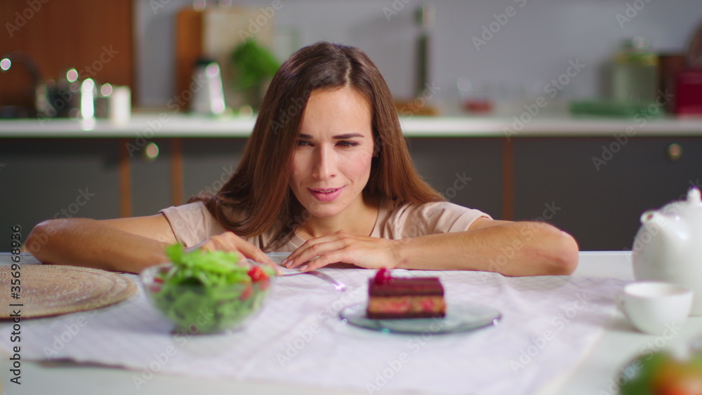 Attractive woman choosing between salad and cake on table. Healthy food concept Attractive woman choosing between salad and cake on table. Healthy food concept