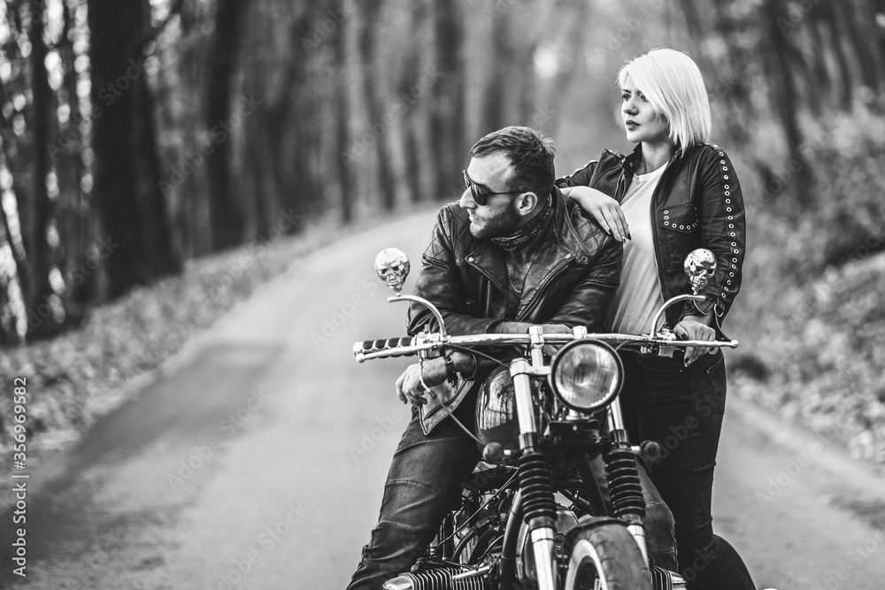 Naklejka premium Pretty couple near motorcycle on the road in the forest with blured background