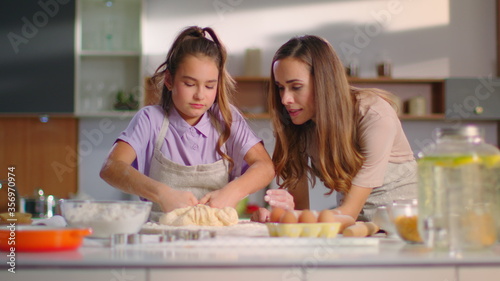 Attractive woman teaching girl to prepare dough for cookies on modern kitchen