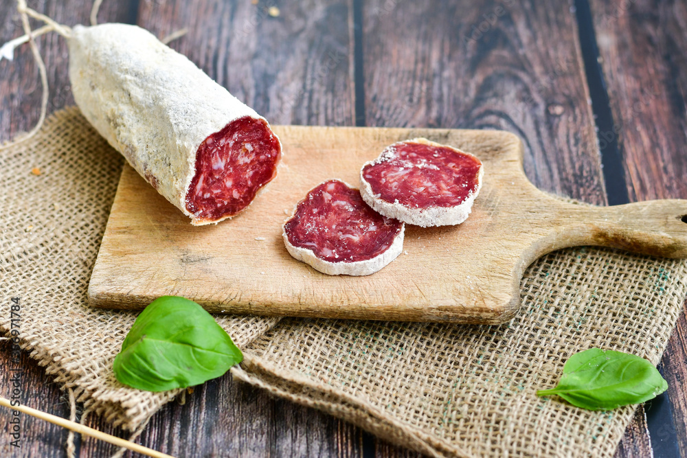 Italian  dried   artisan  pork salami,parmesan cheese ,peperoncino  and fresh basil on wooden background .Rustic  home made food