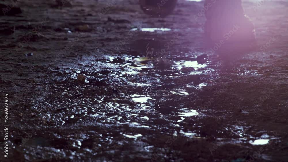 Feet of soldier in army boots moving forward in mud and puddle. Soldier stepping into the muddy puddle at night. The ranger's legs move forward. Steps of a soldier entering an industrial premises