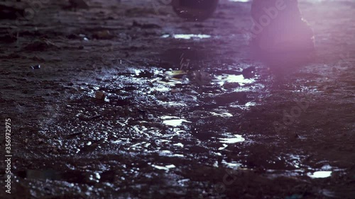 Feet of soldier in army boots moving forward in mud and puddle. Soldier stepping into the muddy puddle at night. The ranger's legs move forward. Steps of a soldier entering an industrial premises