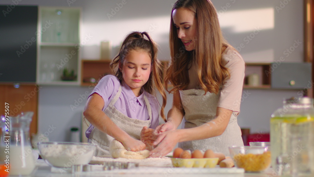 Mother teaching daughter to knead dough for cookies on kitchen in slow motion Mother teaching daughter to knead dough for cookies on kitchen in slow motion